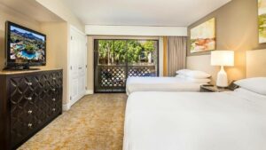 Light hotel room with two beds, a lamp, a dresser, and a tv
